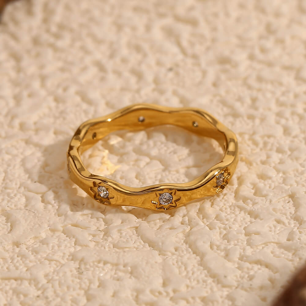 Gold ring band with CZ stones on beige background.
