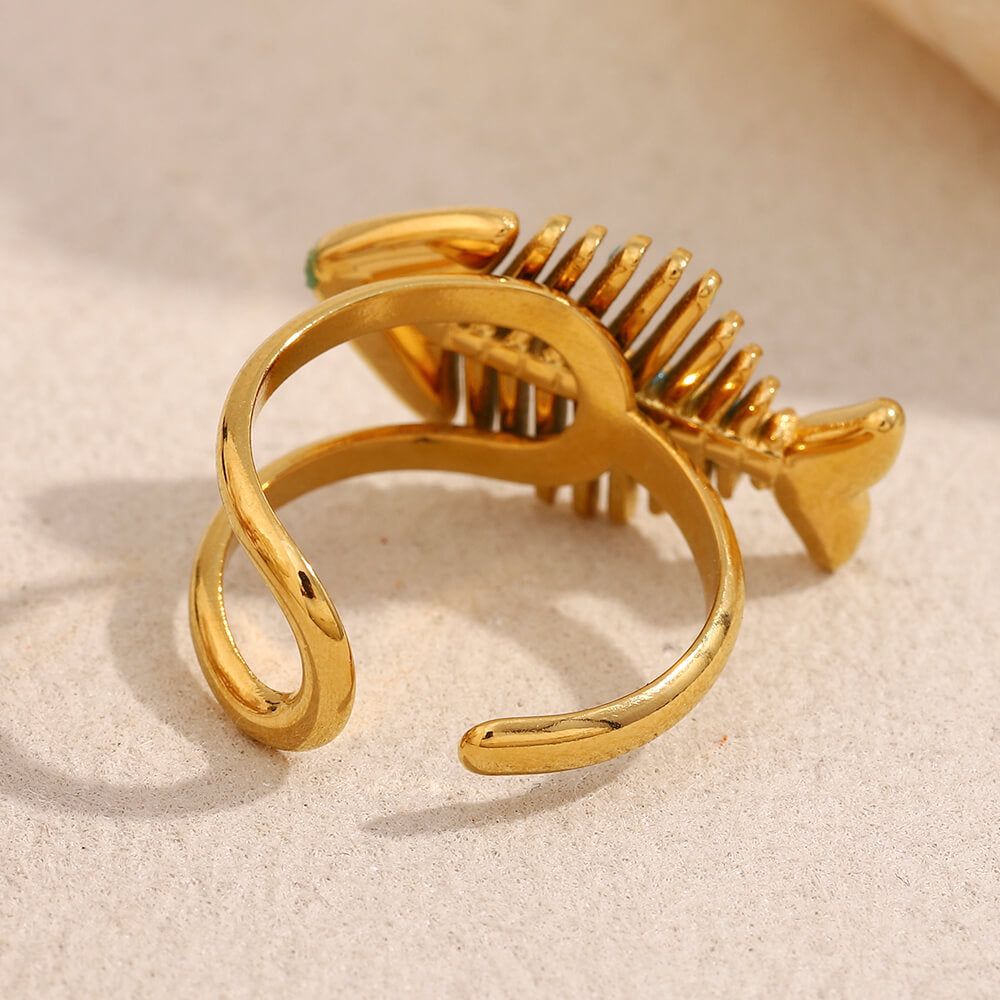 Gold adjustable band fish bone-shaped ring on a beige background.