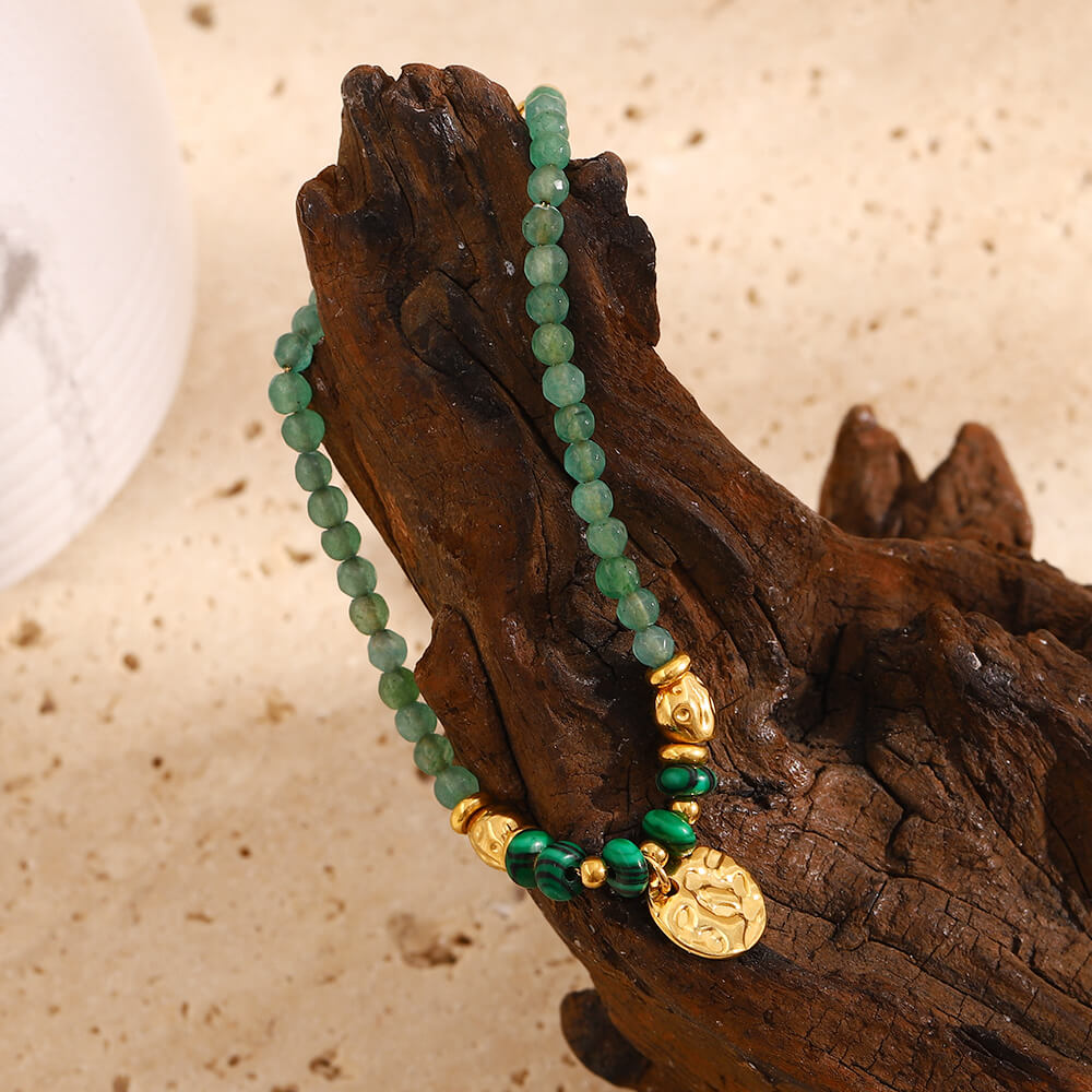 Green and gold beaded bracelet with gold charm on beige background.