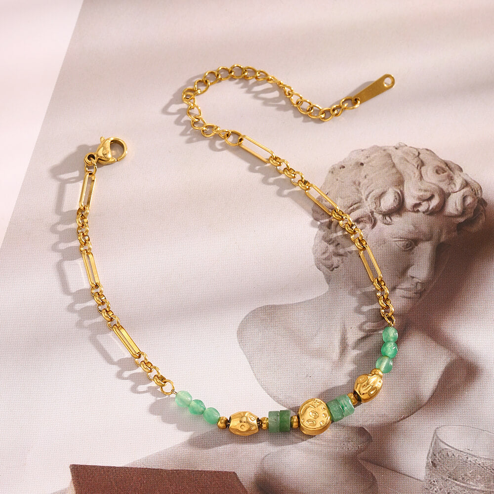 Gold and green beaded bracelet on a classical sculpture background.