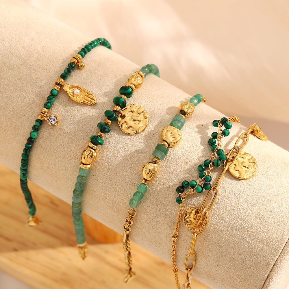 Green beaded and gold bracelet set on a beige surface.