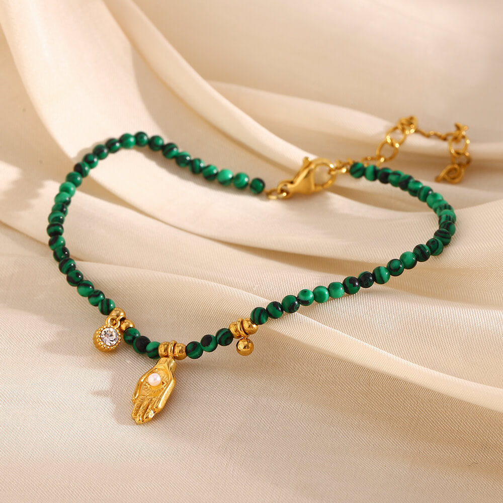 Green beaded bracelet with gold accents on a beige fabric background.