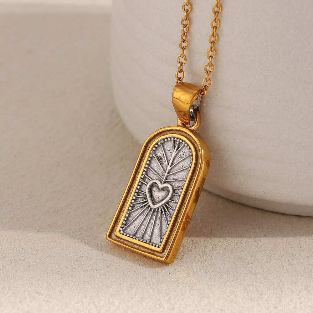 Gold and silver pendant with heart design on a beige background.
