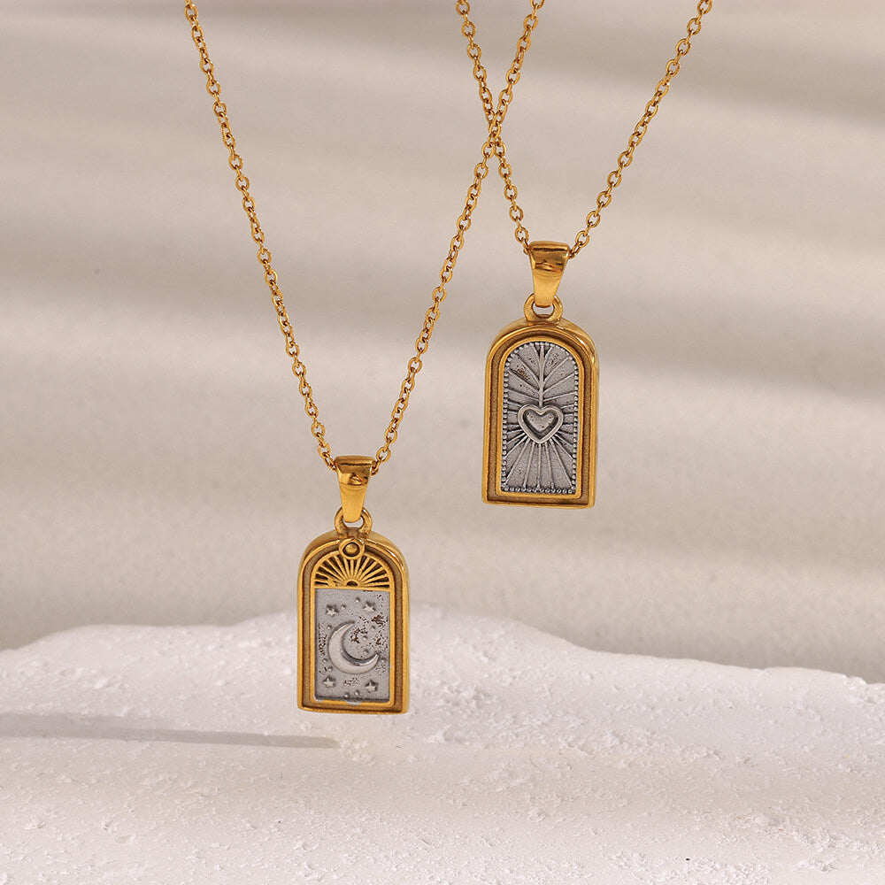 Two gold celestial necklaces with engraved pendants on a textured beige background.