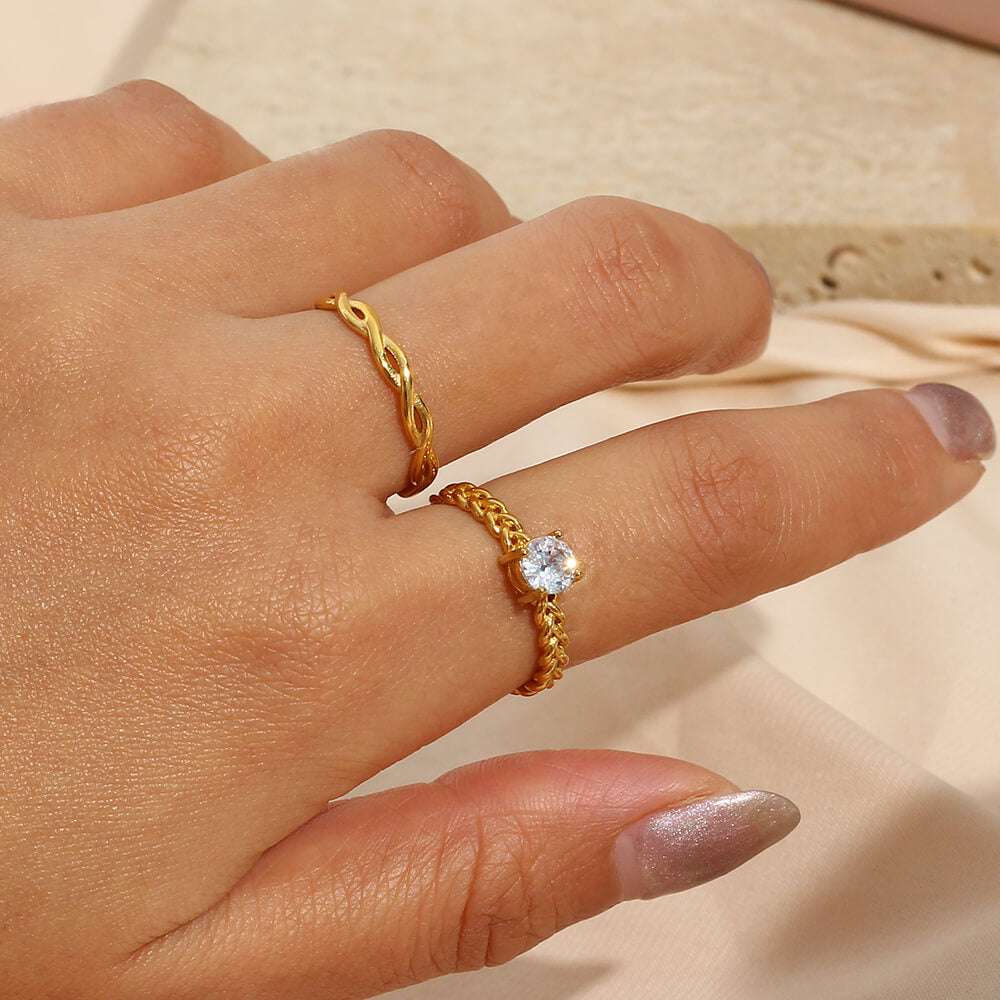 Gold ring with a woven design on a person's finger against a neutral background.