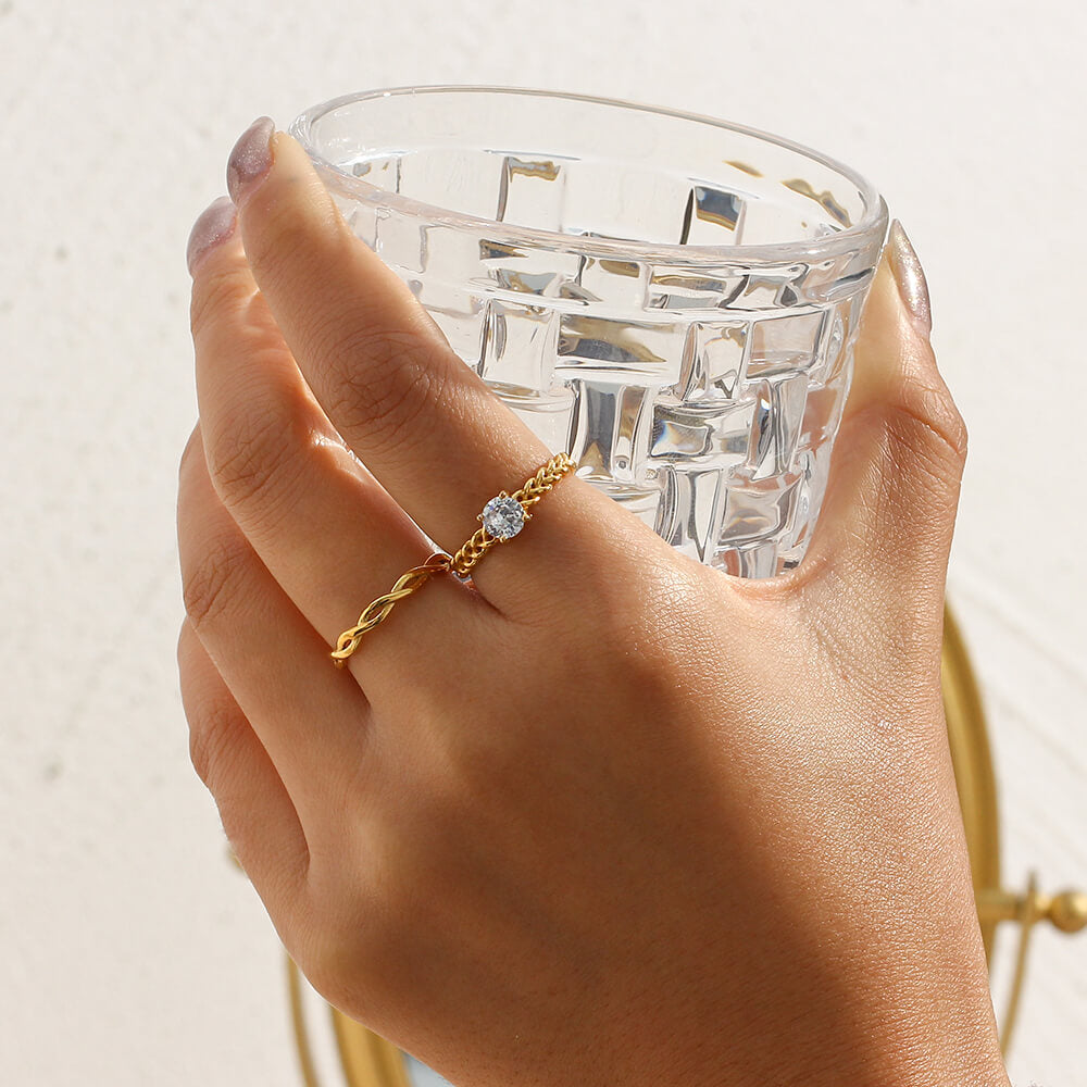 Hand holding a clear glass with a gold ring on a light background.