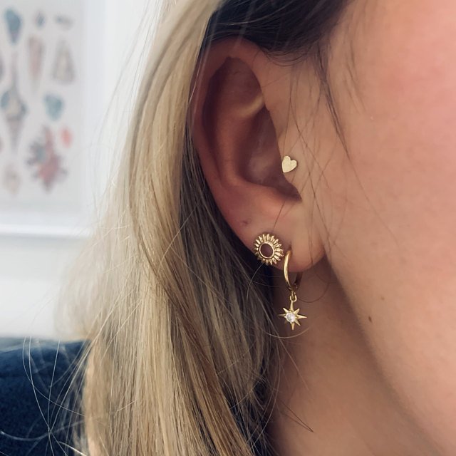 A woman wearing gold star and heart earrings.